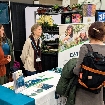 Students speak with attendees of a conference from behind a booth table.