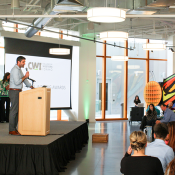 A speaker stands at a podium to present awards to college students.