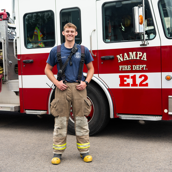 A firefighter poses for a photo in front of a firetruck.
