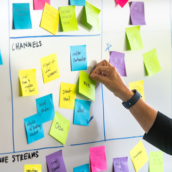 An instructor places a colored post-it note on a white board.