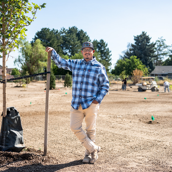 A man stands in a field with newly planted trees and employees working behind him.