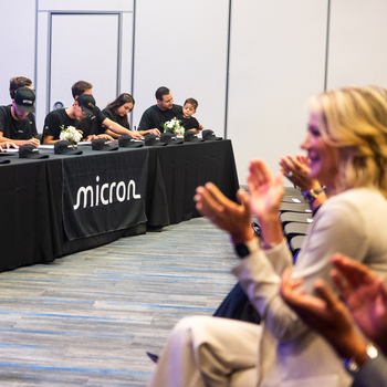New apprentices sign certificates while an audience applaudes.