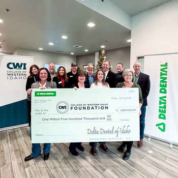 A group of people stand behind a giant check of a donation to a college.