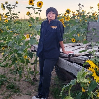 A student stands by an old wagon in a field of sunflowers.