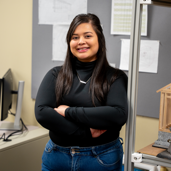 Student stands in front of billboard and next to shelving