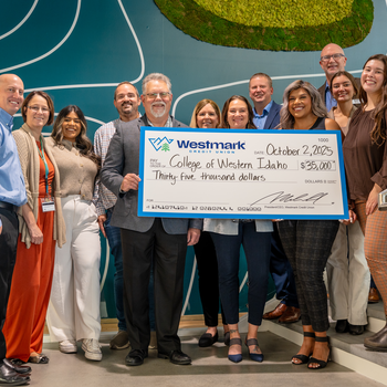 A group of people stand on a staircase smiling and holding a large ceremonial check