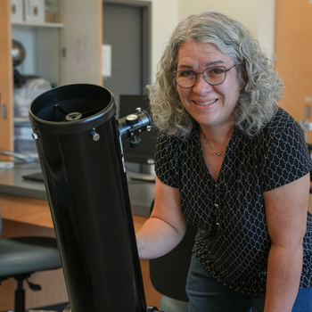 Stephanie Sevigny posing next to telescope in science lab