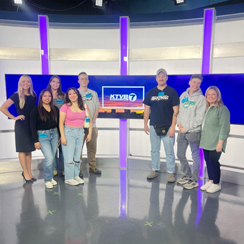 Students touring a TV news station pose for a photo on set. 