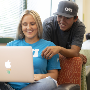 student working on a laptop conversing with another student