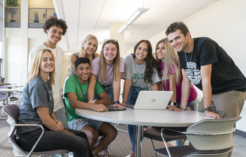 Students gathered around a table on campus smiling at the camera