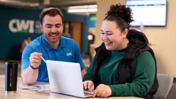 Staff sitting at a table looking at something on a laptop with a student
