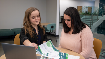 Staff helping a student sitting at a table and looking at papers.