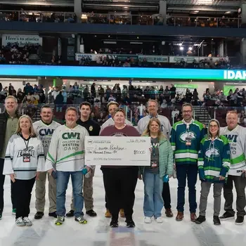 Group of college representatives present a scholarship check on the ice at a hockey arena.