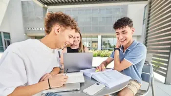 three students studying outside of a campus building at a table