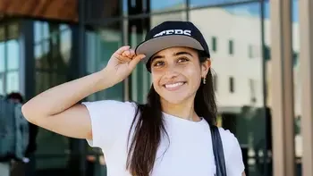 Student wearing an otters hat, outside a campus building, smiling at the camera