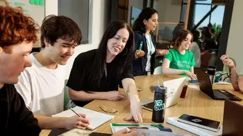 Students sitting at a table discussing things with each other. Books, notebooks, and laptops all over the table.