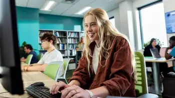 Students studying in a common area inside a campus building at computers and tables