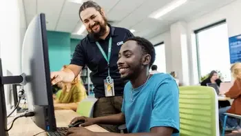 Student at a computer with a staff member helping them