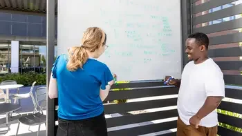 Two students studying and writing out equations on a wipe off board outside on campus