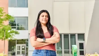 student posing for the camera with arms crossed outside a campus building