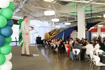 A man standing on a stage addresses an audience at an awards banquet.