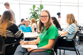 student sitting in common area on campus writing in a notebook