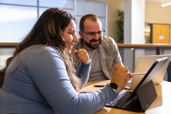 Students helping each other using laptops in a common area on campus