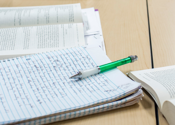 pen on a notebook with handwriting on it next to an open textbook