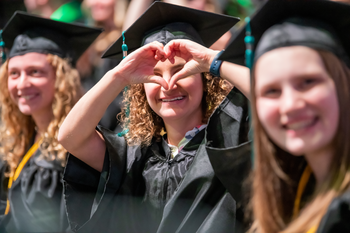 Student in cap and gown making a heart sign with her hands at graduation