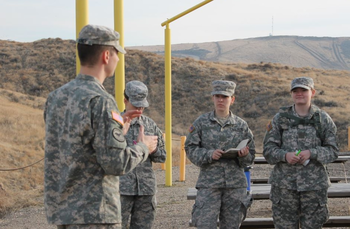Soldiers standing outside by picnic table listening to a presentation
