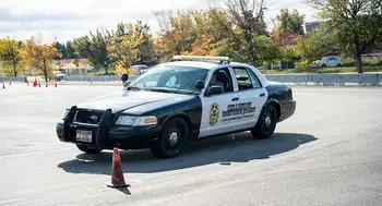A black and white police training vehicle drives through a course marked with orange traffic cones on a sunny day.