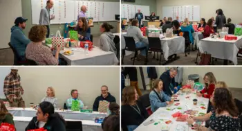 Group of people gathered around tables in a meeting room, socializing and participating in holiday activities.