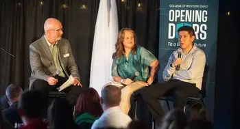 A panel of 3 speakers sit on a stage in front of an audience.