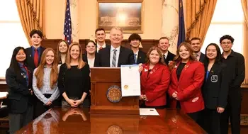 A group of students stand behind the Governor of the State of Idaho as he holds a proclamation. 