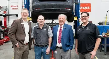 A group photo of people standing in front of a car in an auto garage.