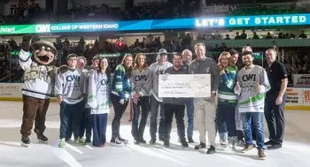 Faculty, staff, and students pose for a group portrait on the ice at a hockey game and holding a ceremonial check.