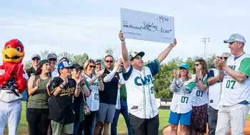 A young man holds up a ceremonial check on the field of a baseball game.