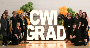 Staff posing in front of a CWI grad light and balloons sign at commencement