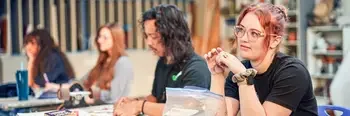 Student in art classroom paying attention to instructor with students in the background working