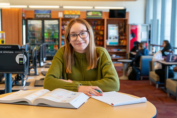 Girl in green sweater studying with books and smiling.