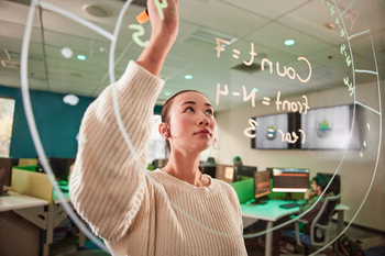 Student solving equation on glass whiteboard.