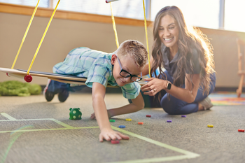 Occupational Therapy Assistant playing with young boy on swing