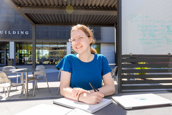 Student smiling and working on schoolwork outdoors.
