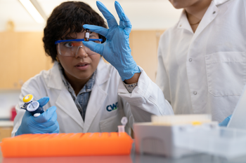 CWI student in safety glasses holding a small substance bottle in a lab