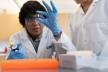 CWI student with safety glasses inspecting a small substance bottle in a lab