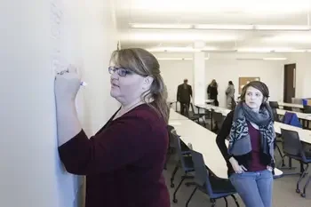 Student writing on white board in front of a classroom