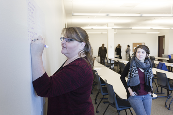 Student writing on white board in front of a classroom