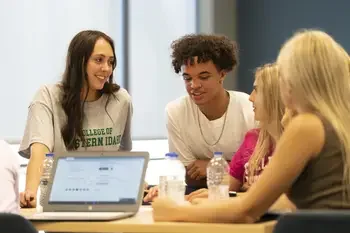 Group of students talking at a table with an open laptop