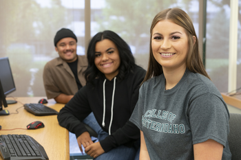CWI students in a computer classroom sitting in a row looking at the camera