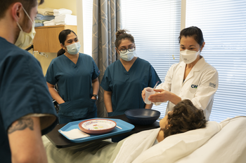 Group of CWI students in a classroom standing over a mannequin's bed